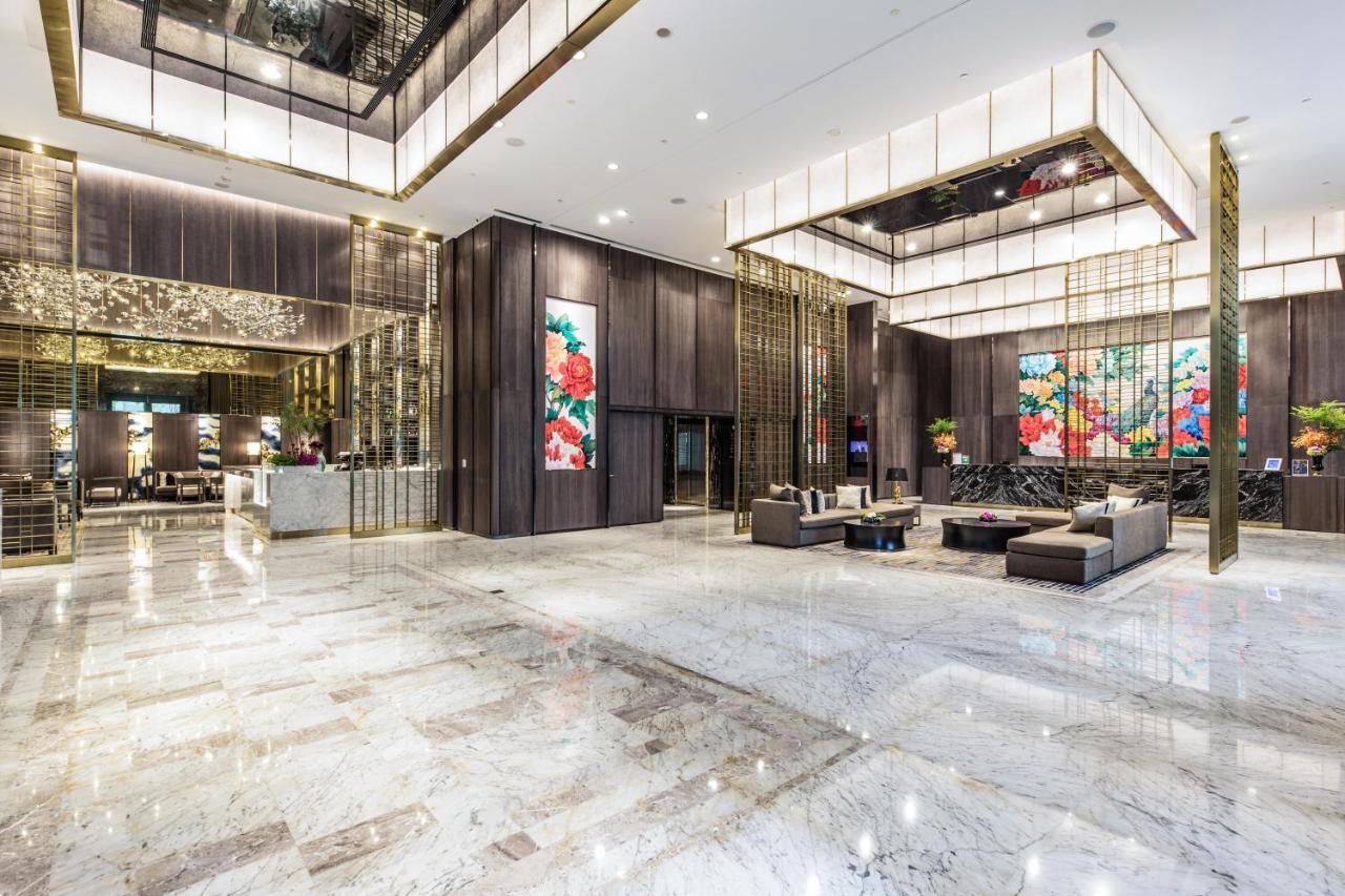 臺北 板桥凯撒大饭店酒店 外观 照片 The photo shows a luxurious hotel lobby. The space features high ceilings with modern architectural design, highlighted by elegant lighting fixtures. On the walls, there are large colorful floral artworks that add a vibrant touch to the space. The fl