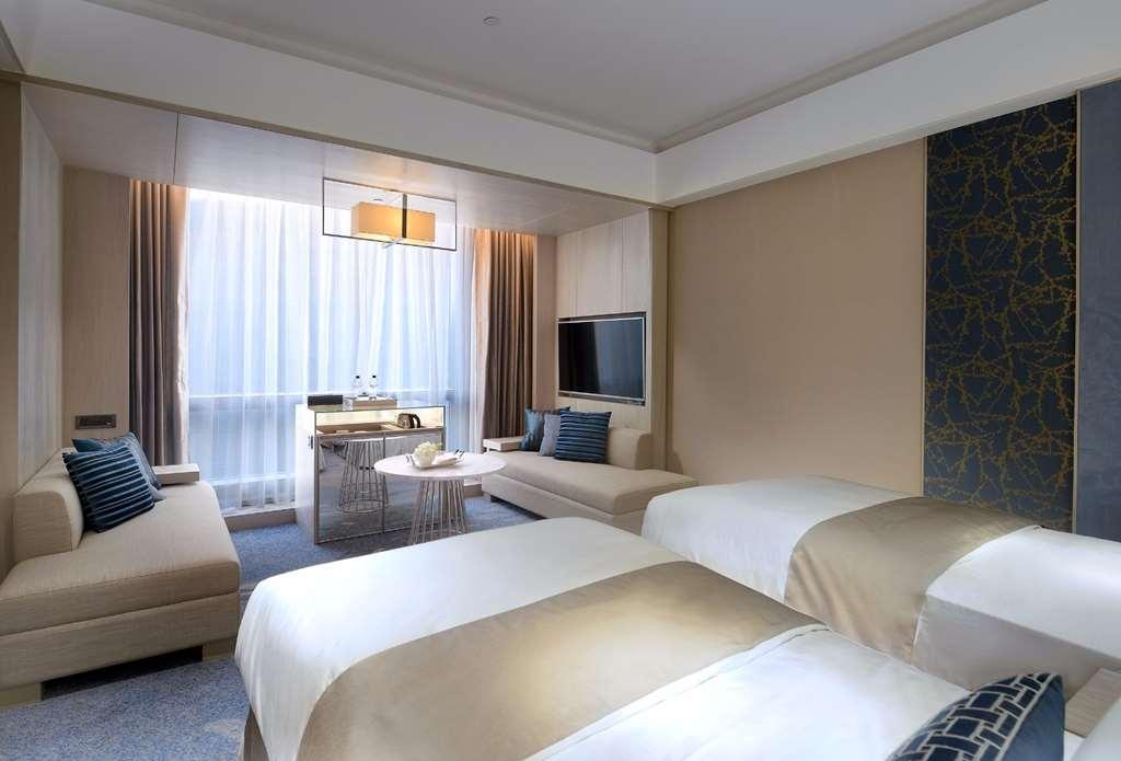 臺北 板桥凯撒大饭店酒店 客房 照片 The photo shows a modern hotel room with a contemporary design. There are two single beds with white linens and beige accents. The room features a large window with sheer curtains allowing natural light to enter, and a small seating area with a couch