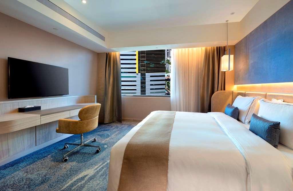 臺北 板桥凯撒大饭店酒店 客房 照片 The photo shows a modern hotel room featuring a large bed with white and beige bedding. There is a comfortable chair by a desk that includes a flat-screen TV mounted on the wall. The room has large windows allowing natural light to enter, with sheer 