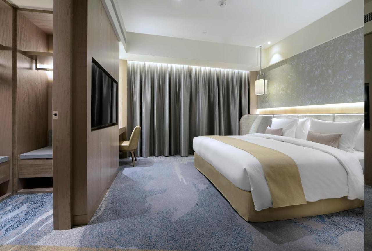 臺北 板桥凯撒大饭店酒店 外观 照片 The photo shows a modern hotel room with a spacious layout. It features a large bed with a light-colored bedspread and pillows, positioned against a sleek wall. The room has a contemporary design with neutral colors and soft lighting. There is a plus