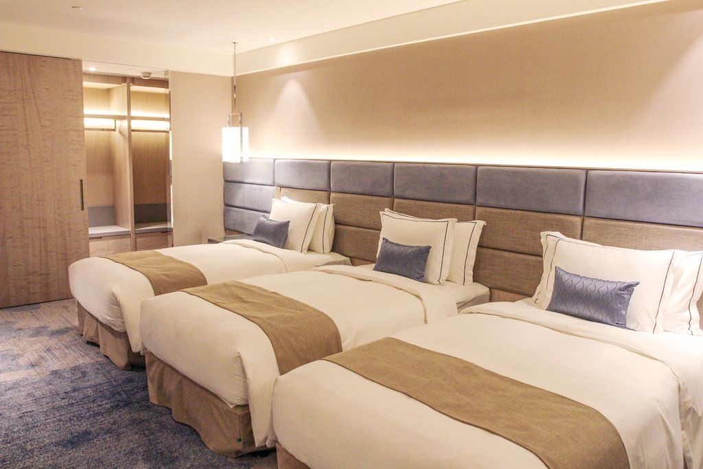 臺北 板桥凯撒大饭店酒店 外观 照片 The photo shows a modern hotel room with three neatly arranged beds. Each bed features a light-colored comforter with a tan stripe running down the center and a decorative pillow in a coordinating shade. The walls are a neutral color, and there is a 