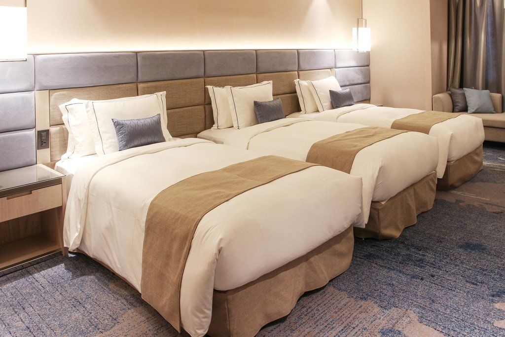 臺北 板桥凯撒大饭店酒店 外观 照片 The image shows a modern hotel room featuring three neatly made beds. Each bed has a cream-colored duvet and a beige throw blanket, along with decorative pillows. The headboard is upholstered in a combination of gray and beige tones. The room has sof