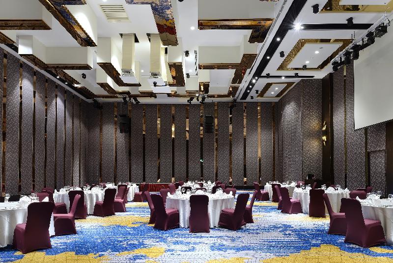 臺北 板桥凯撒大饭店酒店 外观 照片 The photo shows the interior of a large event space or banquet hall. The room features several round dining tables covered with white tablecloths and surrounded by maroon chairs. The flooring has a colorful patterned design, predominantly blue and go