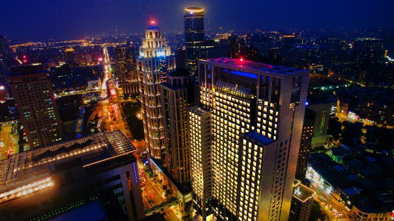 臺北 板桥凯撒大饭店酒店 外观 照片 The photo depicts a nighttime cityscape featuring several tall buildings and skyscrapers. The buildings are illuminated, showcasing bright lights that contrast with the evening sky. You can see streets lined with lights below, suggesting a vibrant ur