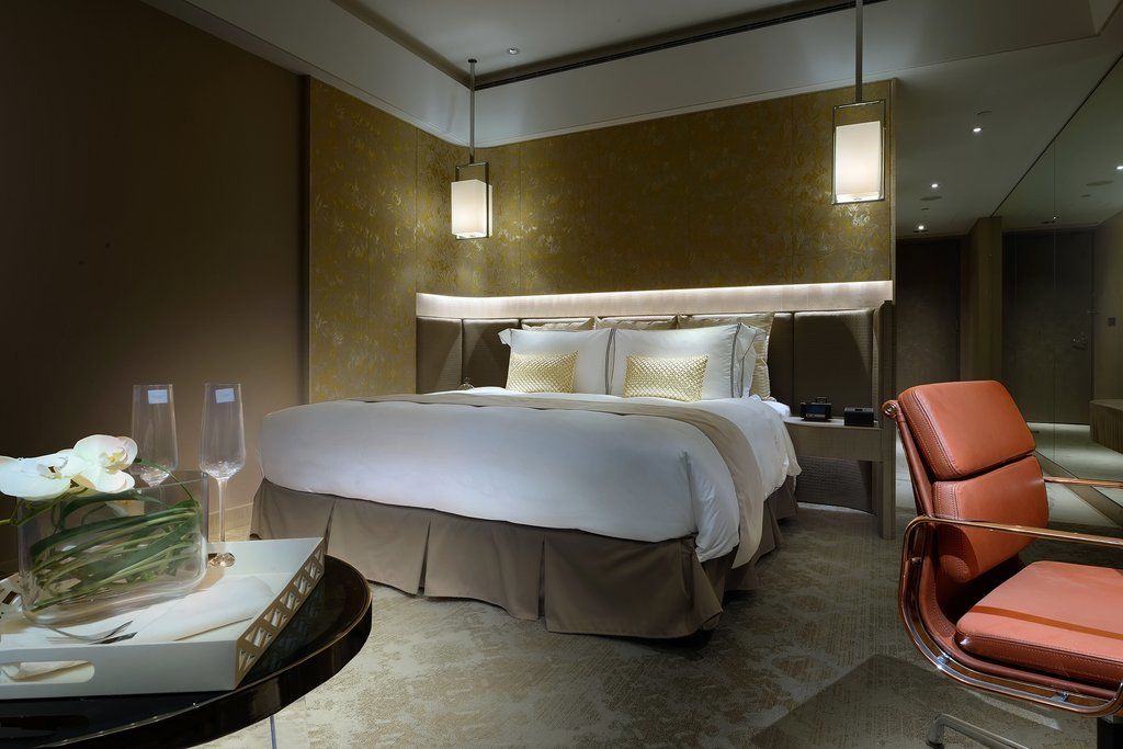 臺北 板桥凯撒大饭店酒店 外观 照片 The photo shows a modern hotel room featuring a large double bed with elegant bedding and decorative pillows. The walls have a warm, neutral tone, complemented by stylish wall lights providing soft illumination. To the side of the bed, there is a con