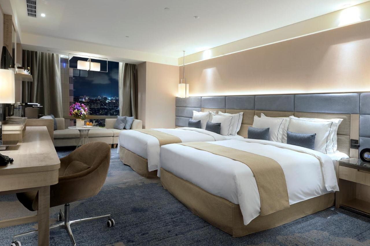 臺北 板桥凯撒大饭店酒店 外观 照片 The photo shows a modern hotel room featuring two twin beds with neutral-colored bedding and plush pillows. The room has a stylish design, including a desk and chair with a contemporary look. Large windows allow for natural light and offer a view of 