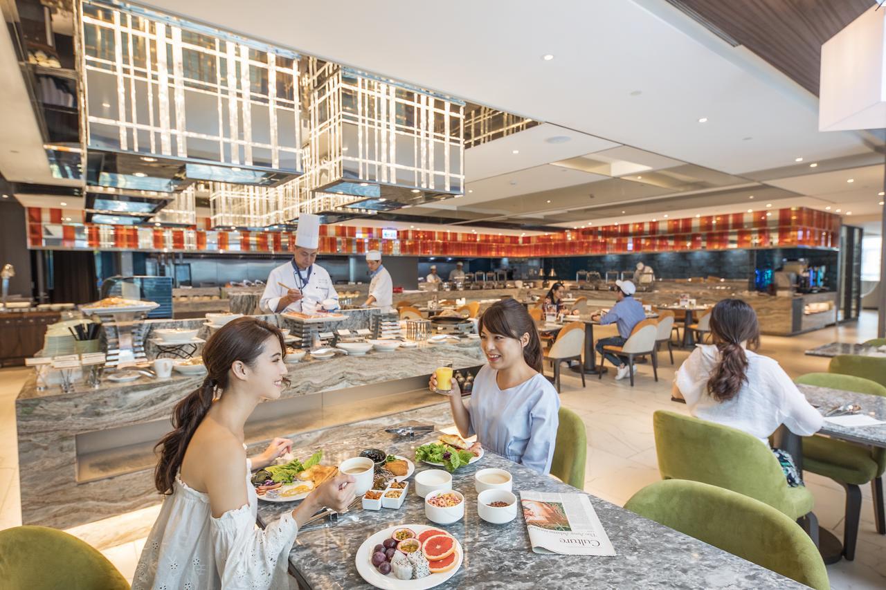 臺北 板桥凯撒大饭店酒店 外观 照片 The photo depicts a modern restaurant setting with a contemporary design. In the foreground, two women are seated at a table, enjoying their meals and engaging in conversation. Their table is set with an array of food items, including fruits, salads,