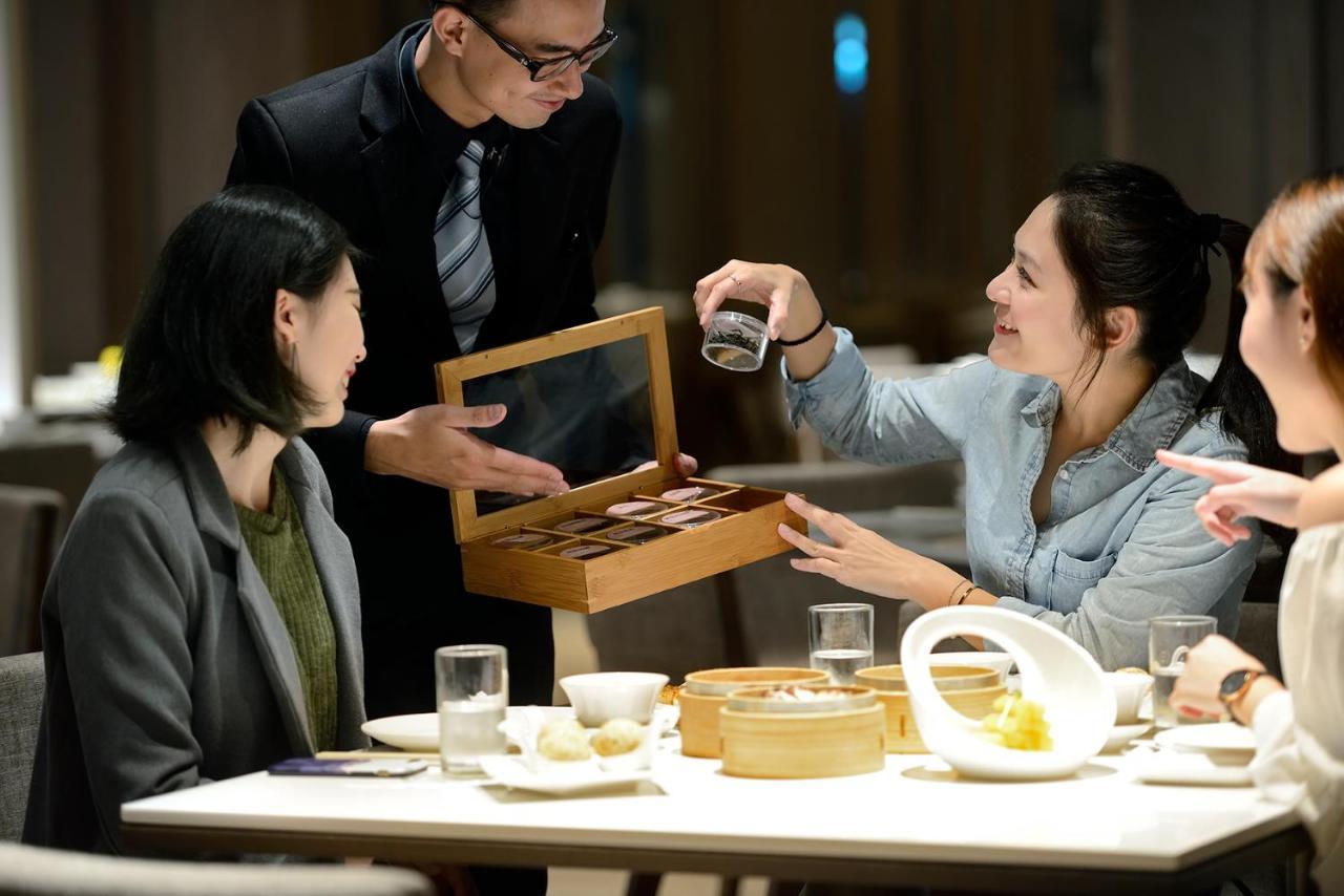 臺北 板桥凯撒大饭店酒店 外观 照片 The photo shows a dining scene in a restaurant. A waiter is presenting a wooden box containing tea or desserts to a group of women seated at a table. One of the women is reaching out to take something from the box, while the others are engaged in con