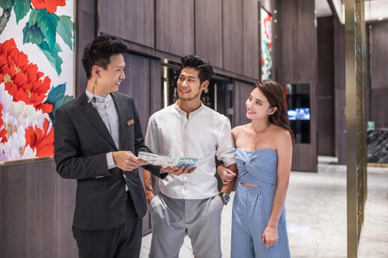 臺北 板桥凯撒大饭店酒店 外观 照片 The photo shows three individuals interacting in a modern, upscale setting. One person, dressed in formal attire, appears to be providing information or assistance, possibly in a hospitality context. The other two individuals, a man and a woman, are 